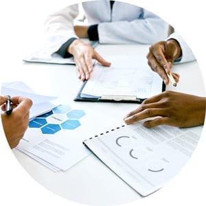 Paperwork featuring charts and tables being discussed around a table.