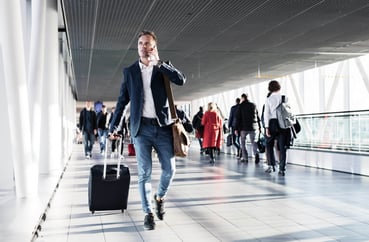 Male passenger with suitcase talking on the phone on the way to his gate. 